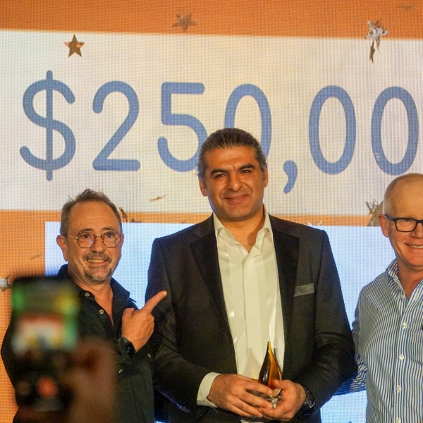 Three men standing on stage in front of a sign that reads "$250,000"