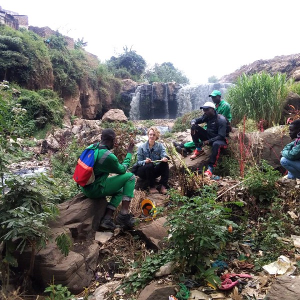 Kate Chesebrough sits with four youth group members near a small waterfall and stream.