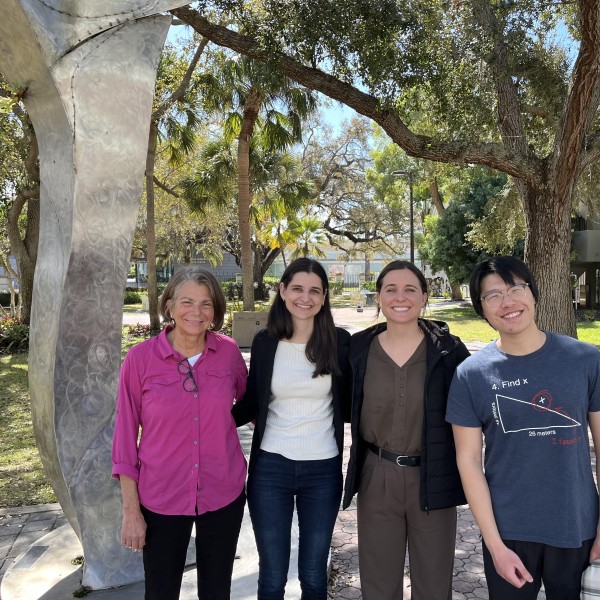 4 individuals standing, smiling with trees in the background