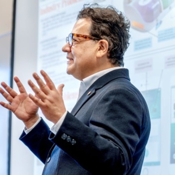 Juan Hinestroza speaking in front of a projecter screen. 