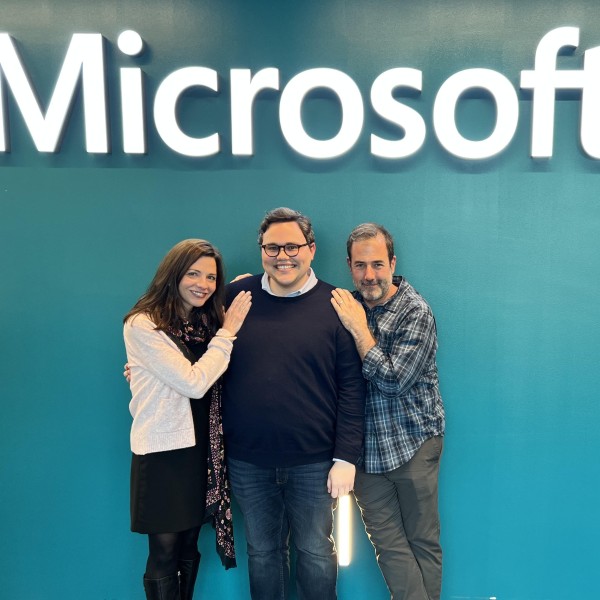 3 individuals pose for a picture in front of Microsoft logo
