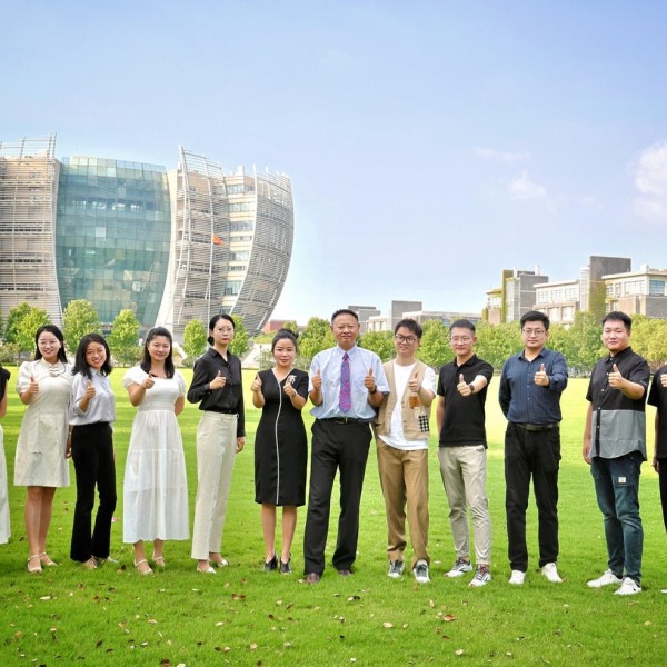 team of people standing in open grass field in front of large building