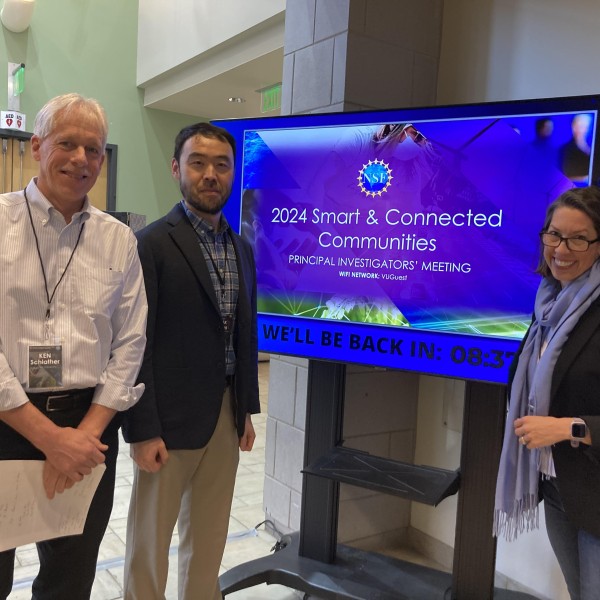 3 people stand in front of TV screen smiling
