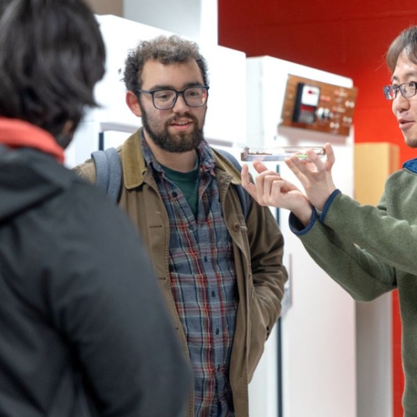 Two men, in a green and grey jacket, speak with two students.
