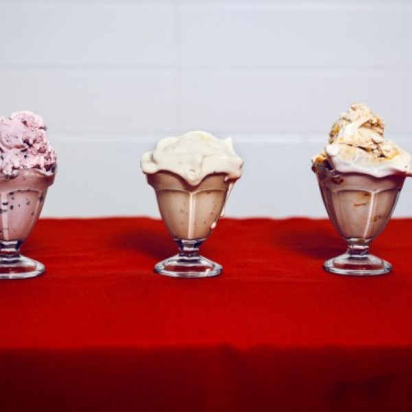 Three ice cream dishes on a red table. From left to right, a pink spotted ice cream, a white gooey ice cream, and a golden white ice cream.
