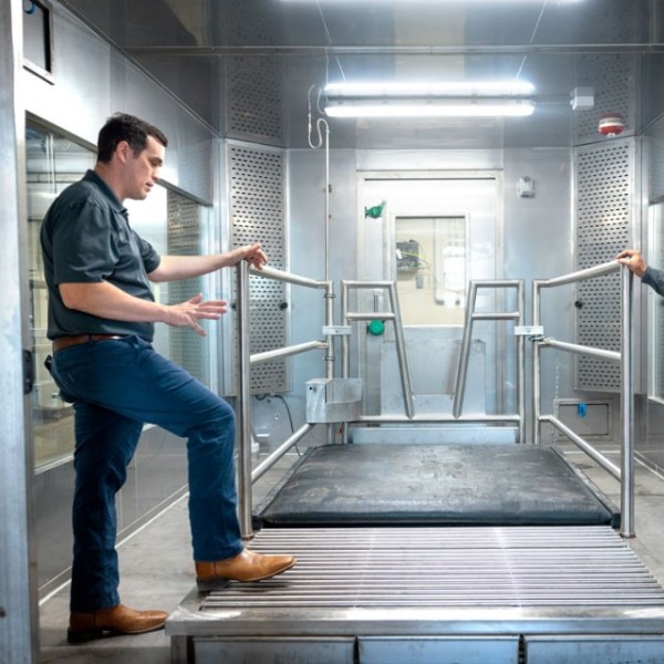 Two men speak inside of a large room with metal walls.