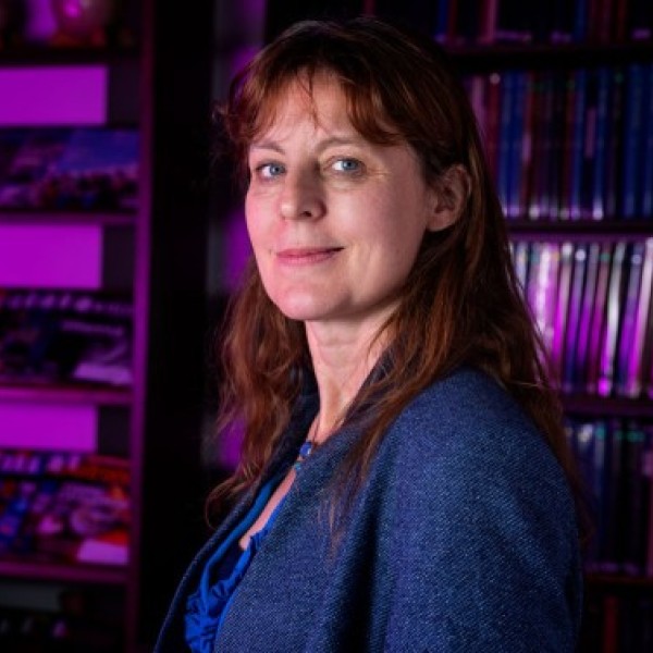 A woman stands in front of a bookshelf washed in purple light.