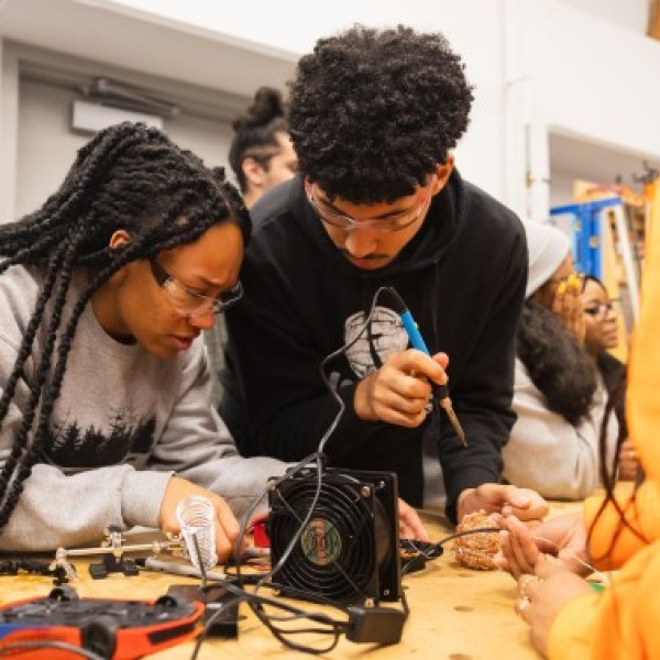 Two students, a man and a woman, use a soldering iron to rewire a toy.