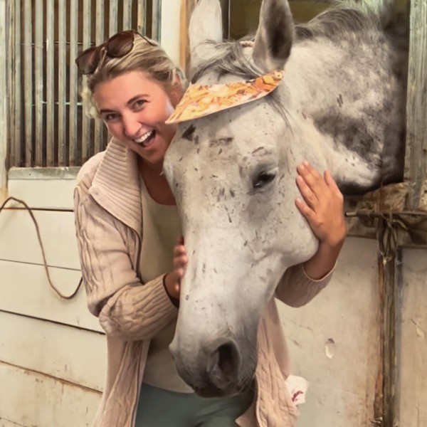 a woman hugs the head of a horse peering out of its stall