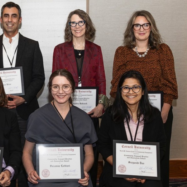 Eight people, two men and six women, in colorful tops, sit for a group photo with their award certificates that read "Community-Engaged Practice and Innovation Award"