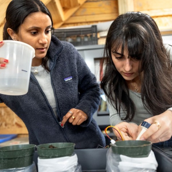 Two female students hold plastic containers and examine circuitry. 