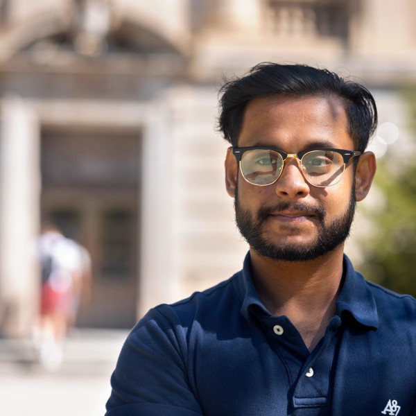 A headshot of Talha Islam, in front of a stone building, Warren Hall.