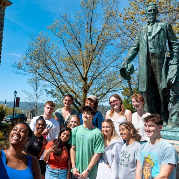 A group of students take a photo in front of the Ezra Cornell statue on the Arts Quad. 