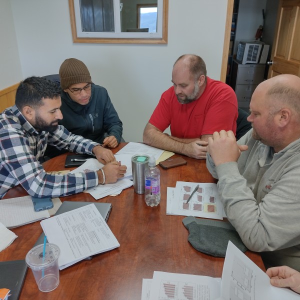 Four men sit around a table looking at project paperwork.