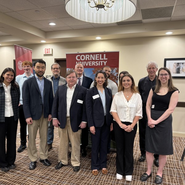group of individuals standing and smiling in front of Cornell University sign