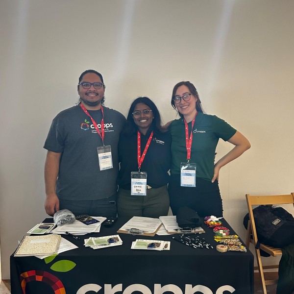 three individuals stand behind table smiling at conference