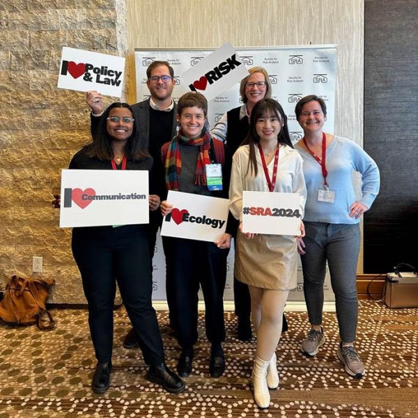 Alumni pose in front of photo op with signs