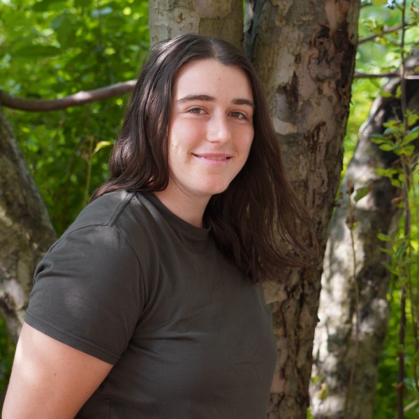 A woman standing in front of a tree smiling.