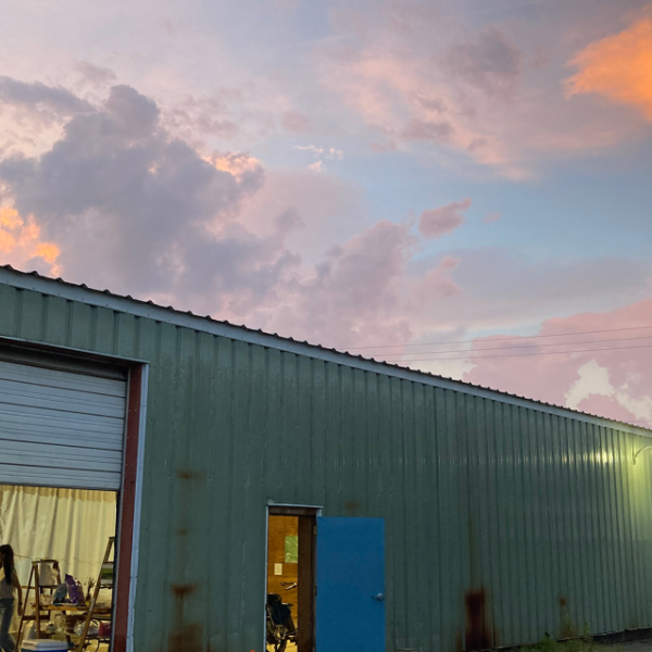 Metal-sided garage space with door rolled up and people inside working at a table