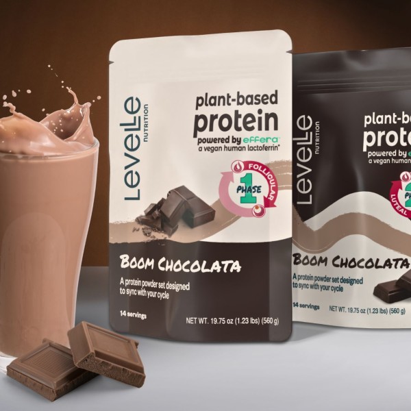 Two bags that say "Plant-based protein" and "boom chocolata" next to a glass of chocolate milk.