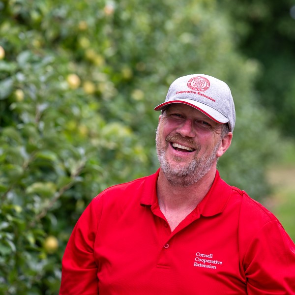 Man stands in front of apple orchard smiling