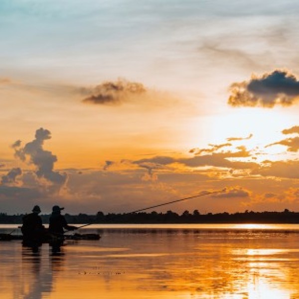 Two fisherman on a small boat cast fishing lines into the water at sunset