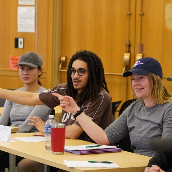 Two people gesture to the left while sitting at a table with a paper placard reading "regulatory agencies."