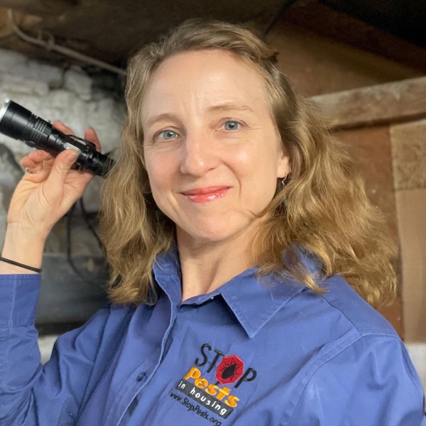 Susannah Krysko holding a flashlight and smiling, wearing a stop pests shirt