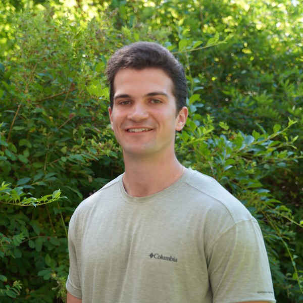 A man smiles in front of a background of greenery.