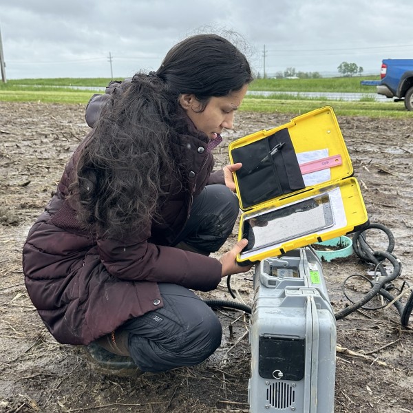 A woman crouches in a field looking at a tablet housed in a case.