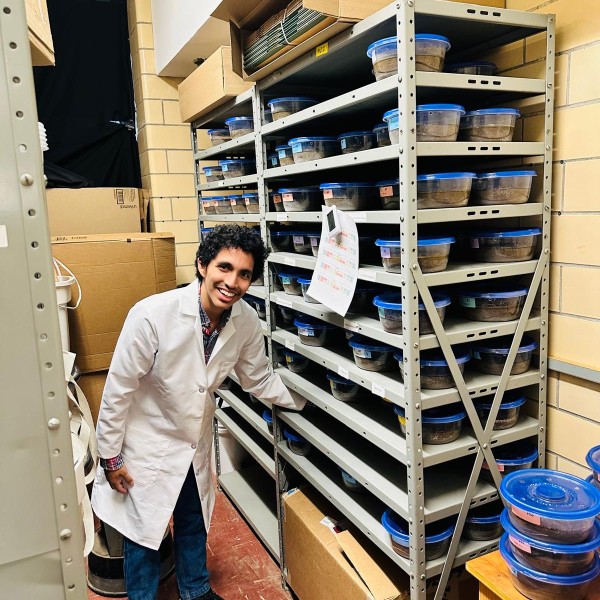 A man reaches onto a shelf. He is wearing a lab coat.
