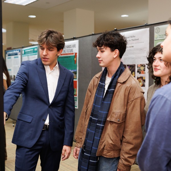 A student reads off a poster with three other students gathered around listening. 