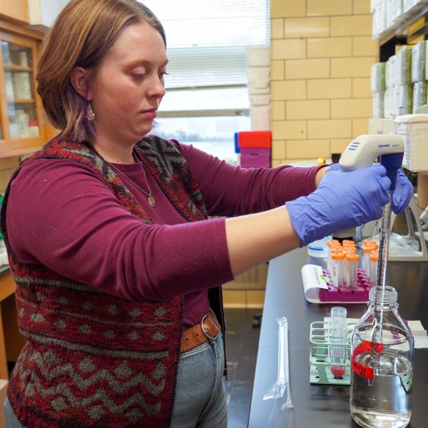 a woman sucks up fluid with a pipette in a lab