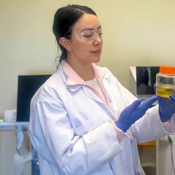 a woman in a lab coat looks at a beaker of liquid