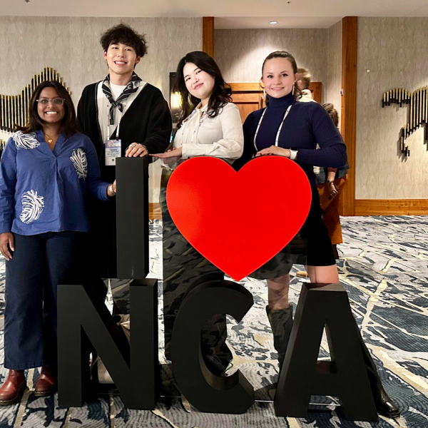 four people stand in front of a sign that reads I heart NCA