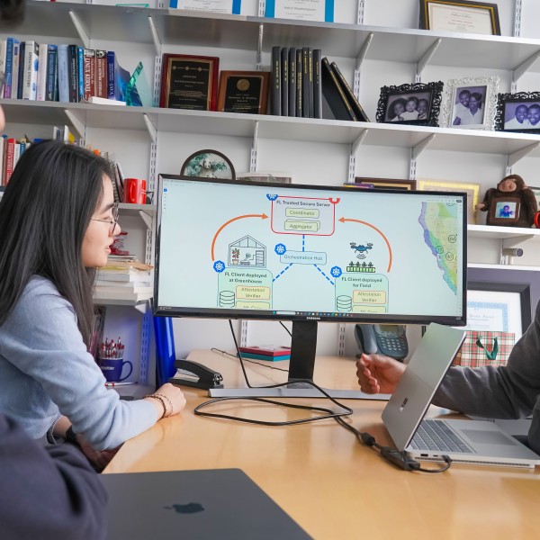 two men and a woman sit at a table talking with a schematic of farm and data on a view screen next to them