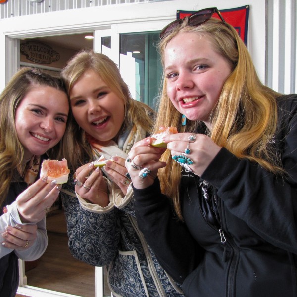 three woman stand together eating orange slices