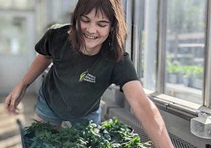 Smiling woman tends plants in greenhouses.