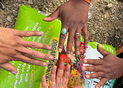 four hands coming together over a bag of soil