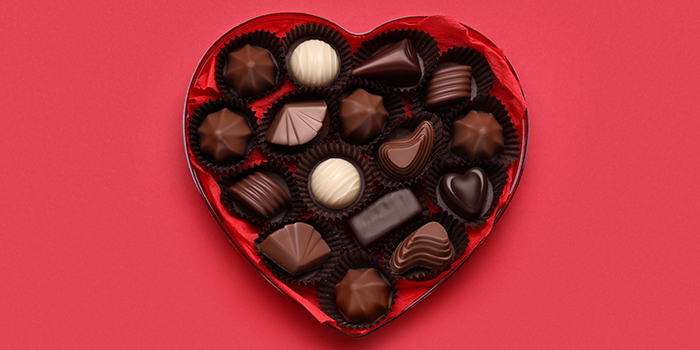 Heart shaped box with delicious chocolate candies on red background, top view